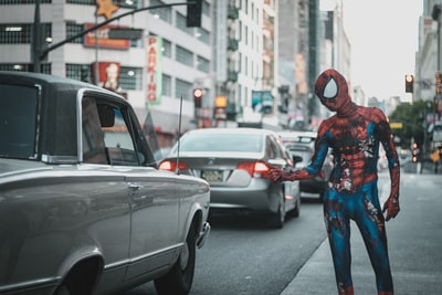 穿着蜘蛛侠服装的男人站在人行道上，车停在路上